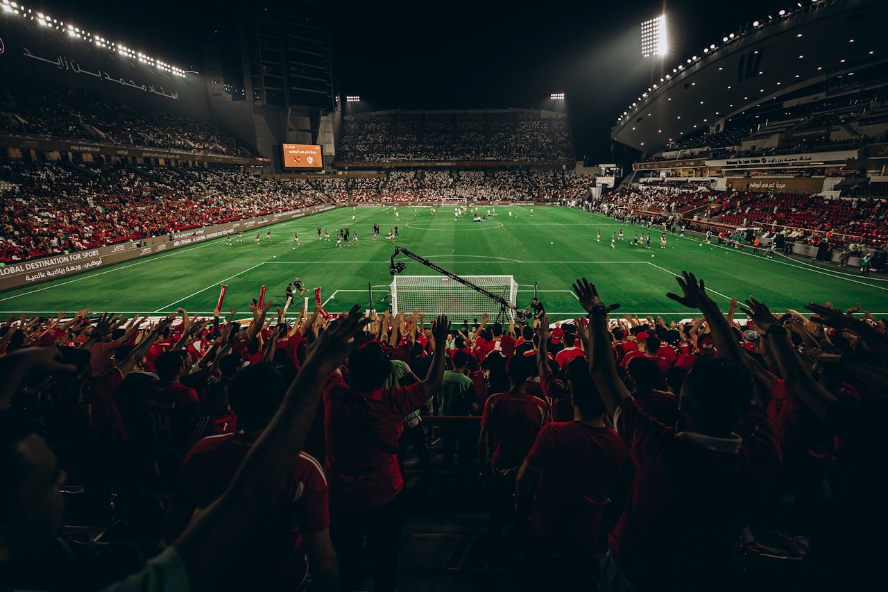 Aerial view of a vibrant football match in a packed stadium at night, capturing the excitement of sports fans.